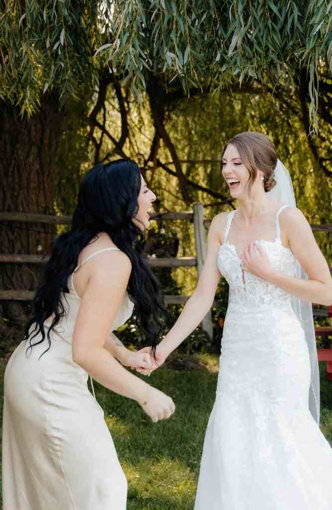 A bride laughing with her maid of honour in a candid photo at Summerhill Winery in the Okanagan