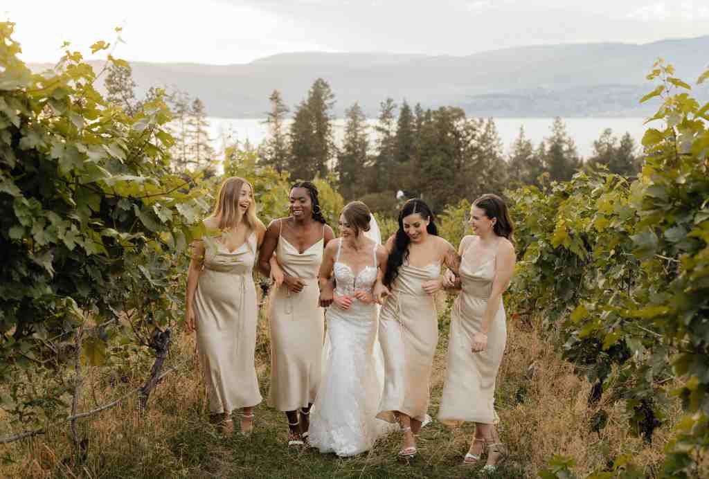 A bride and her bridesmaids walking and laughing in the vineyard at Summerhill Winery in Kelowna, BC - shot requested in the bride's wedding shot list