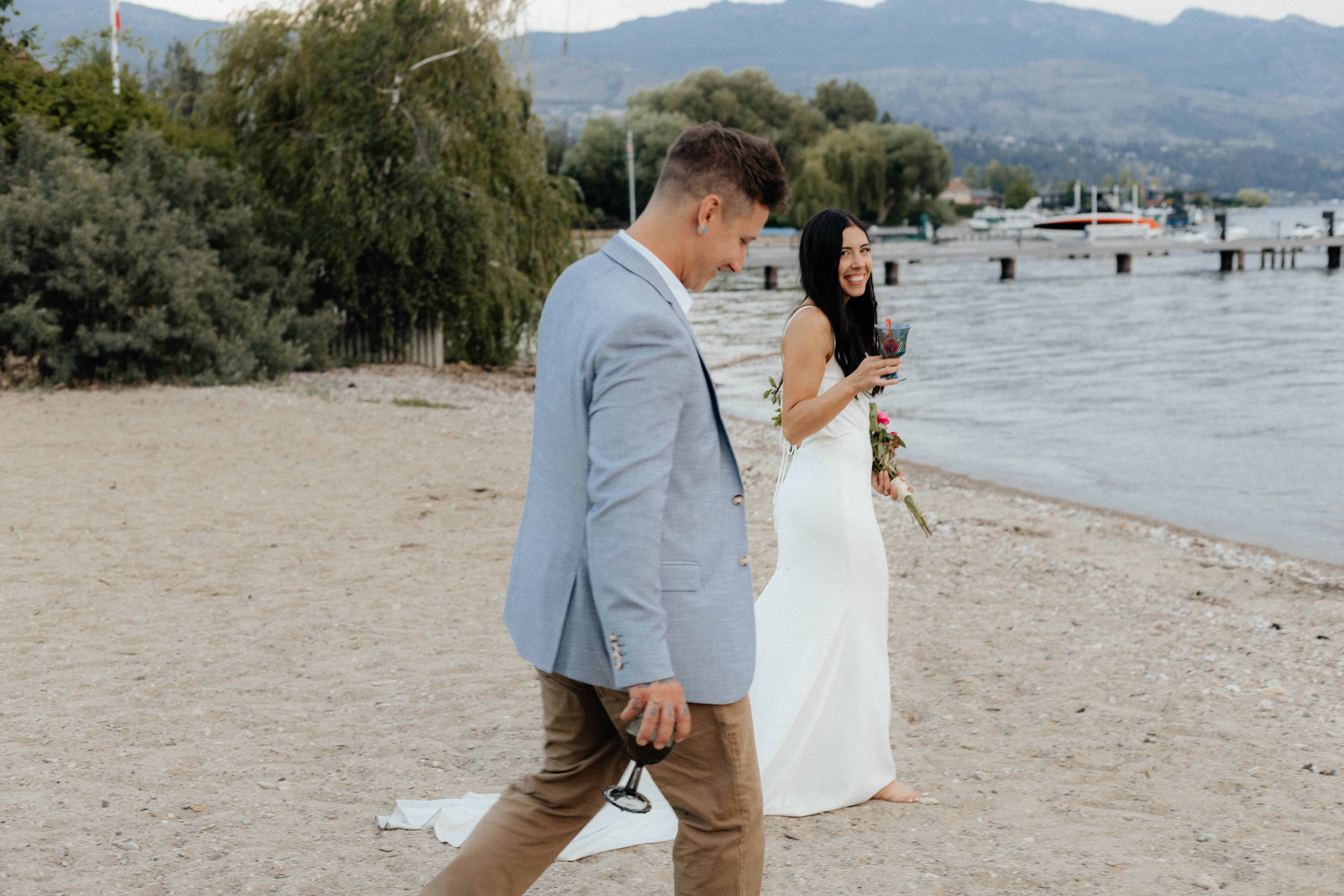 Candid photo of a newlywed couple strolling on the beach at Lake Okanagan
