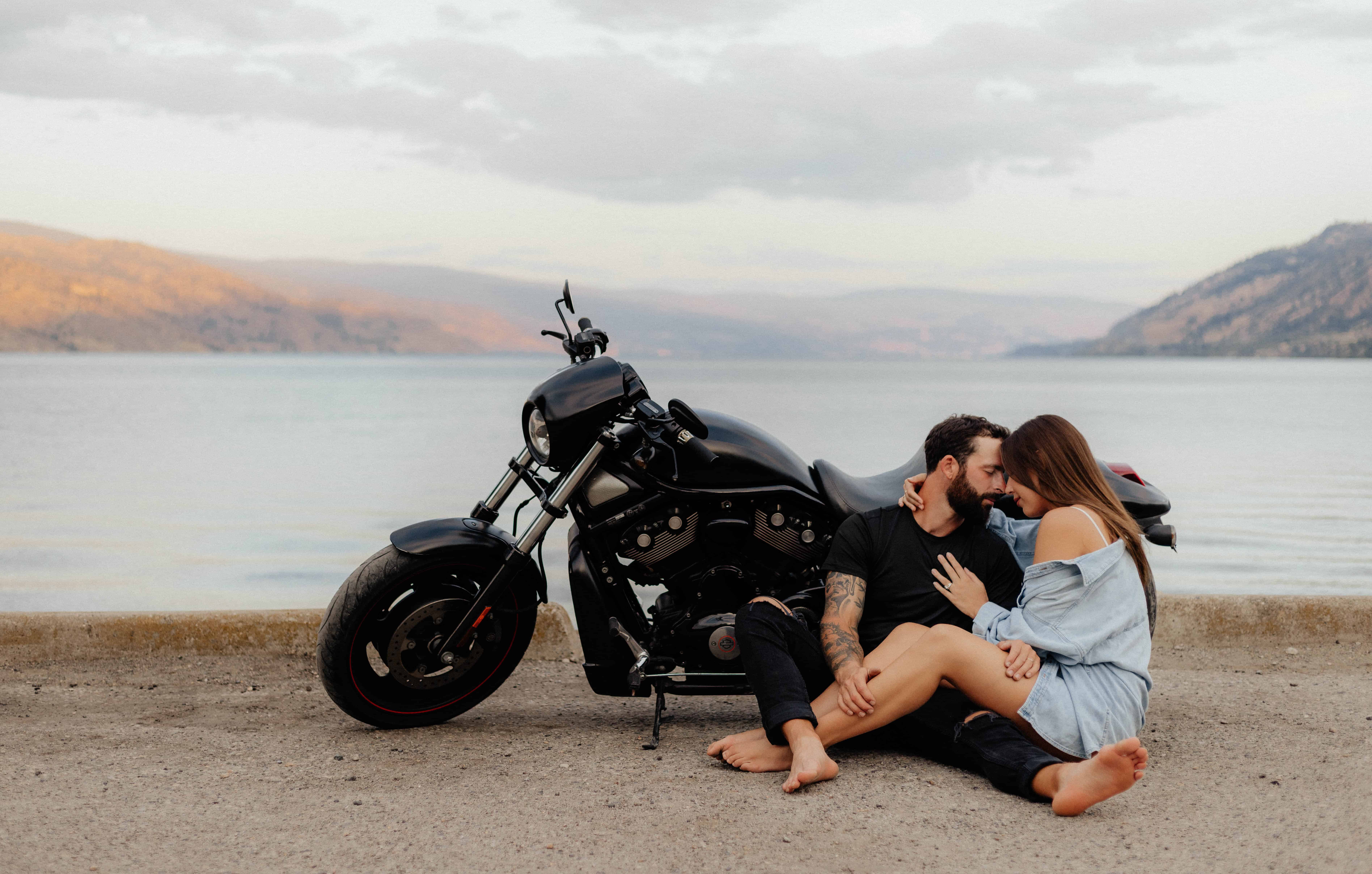 A beautiful couple poses with their motorcycle in front of lake Okanagan