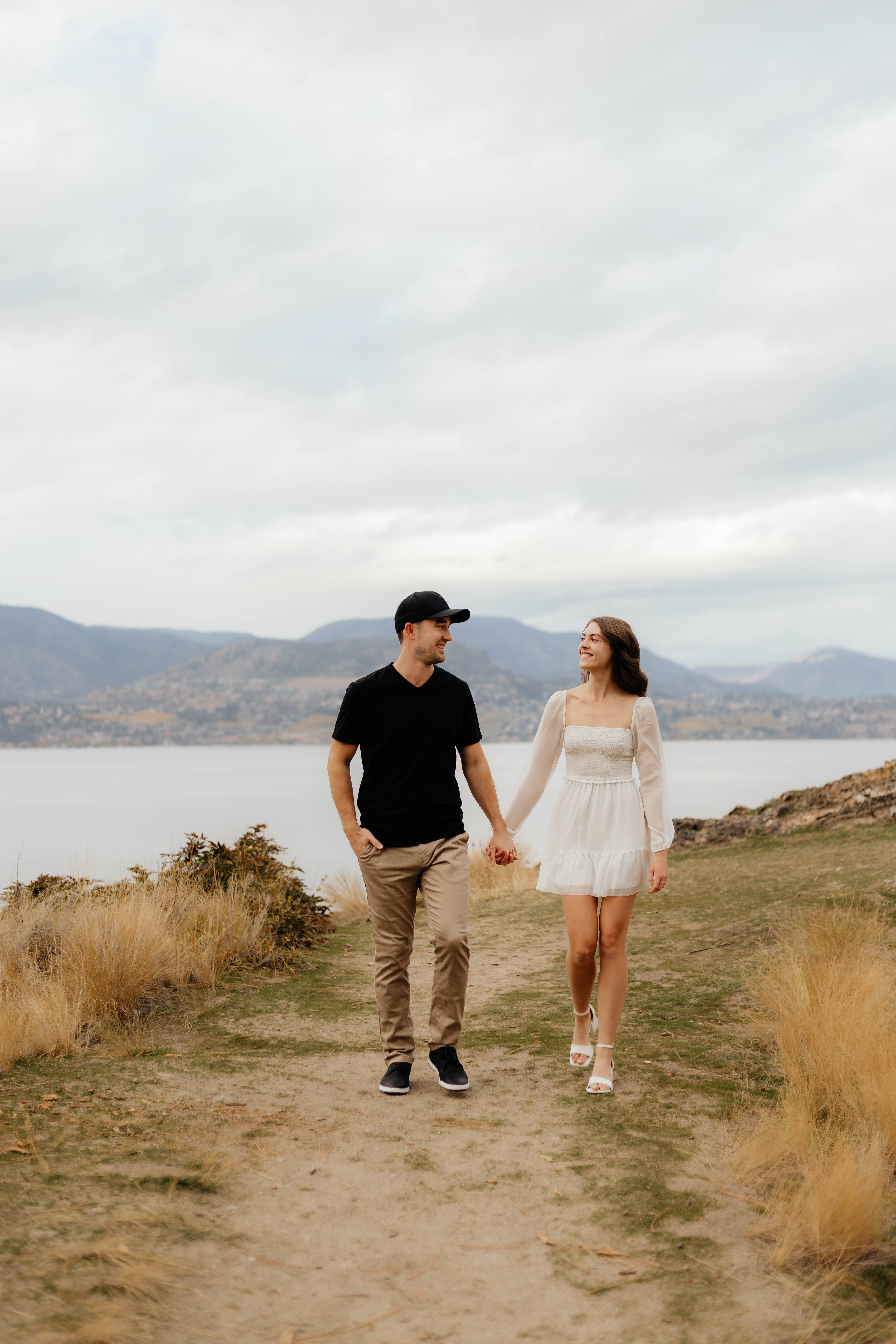 A beautiful happy couple walks hand in hand during their engagement photoshoot overlooking Lake Okanagan