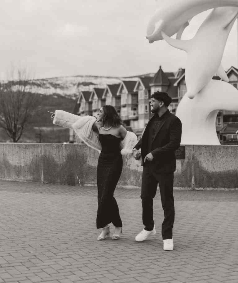 A couple laughing and walking hand in hand while pointing at something hilarious out of frame in downtown Kelowna