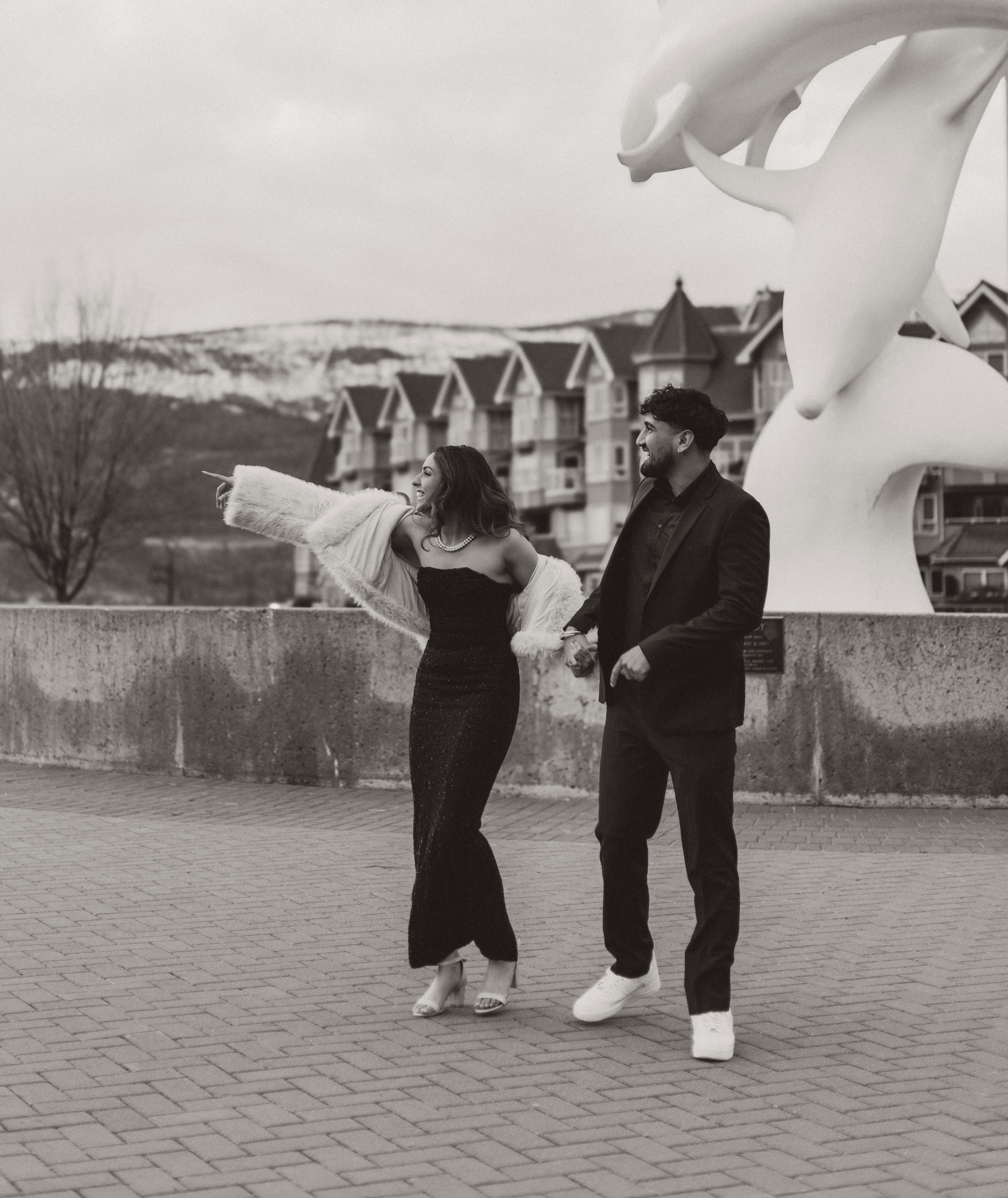 A couple laughing and walking hand in hand while pointing at something hilarious out of frame in downtown Kelowna