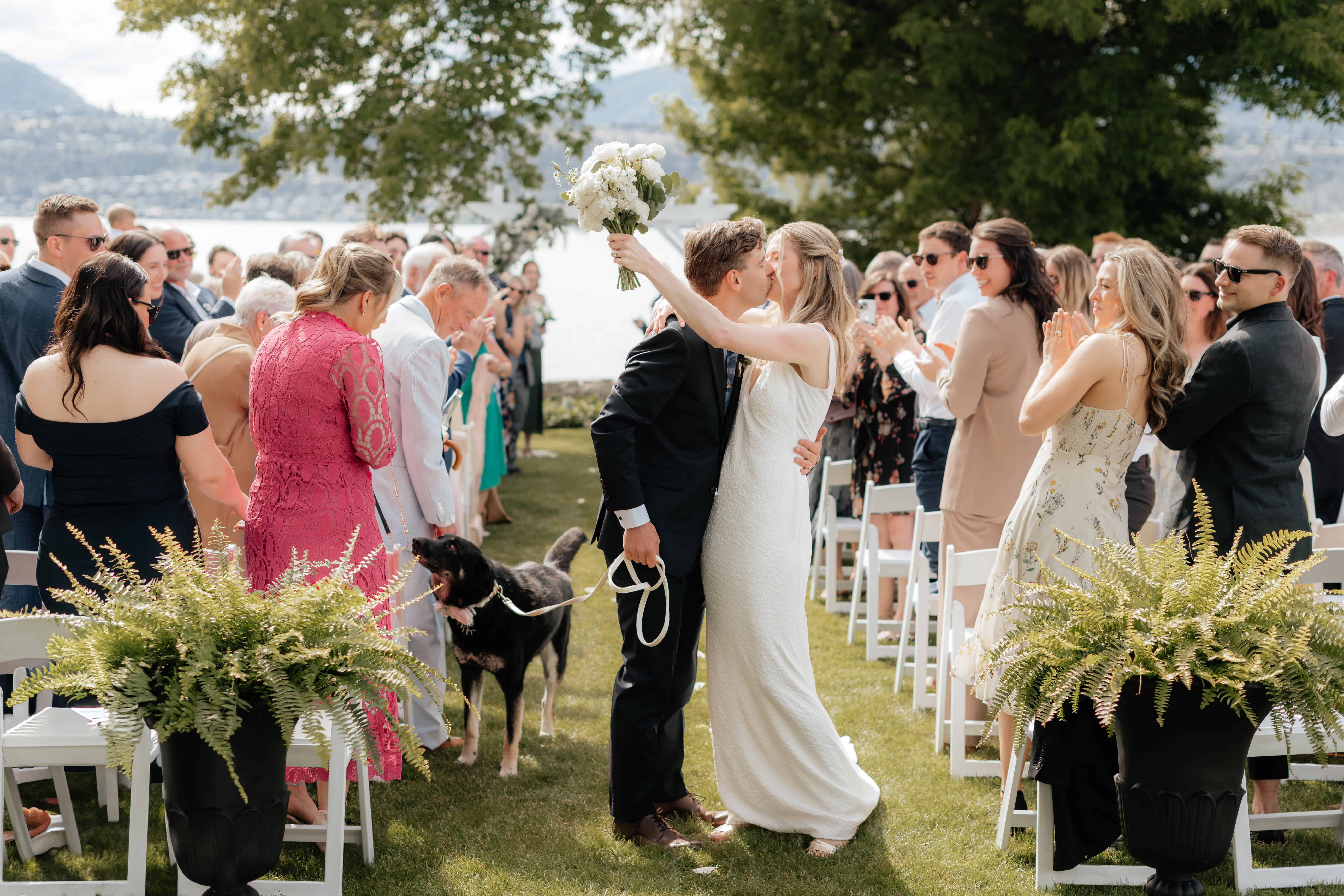 A bride and groom kiss at the end of the aisle after tying the knot in a beautiful backyard ceremony in Kelowna, BC