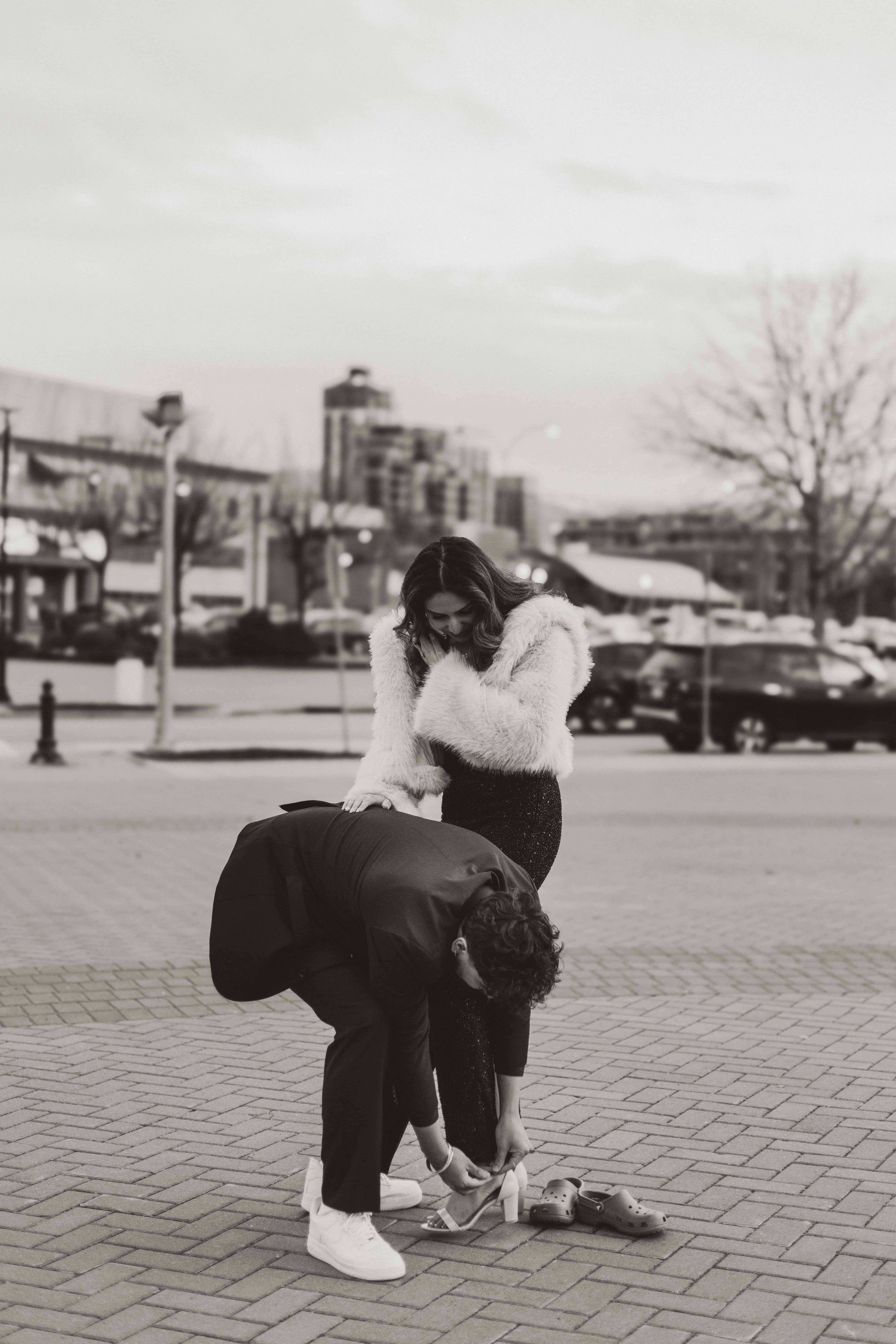 A man helps a woman buckle her shoe in front of Prospera Place near the lake in downtown Kelowna