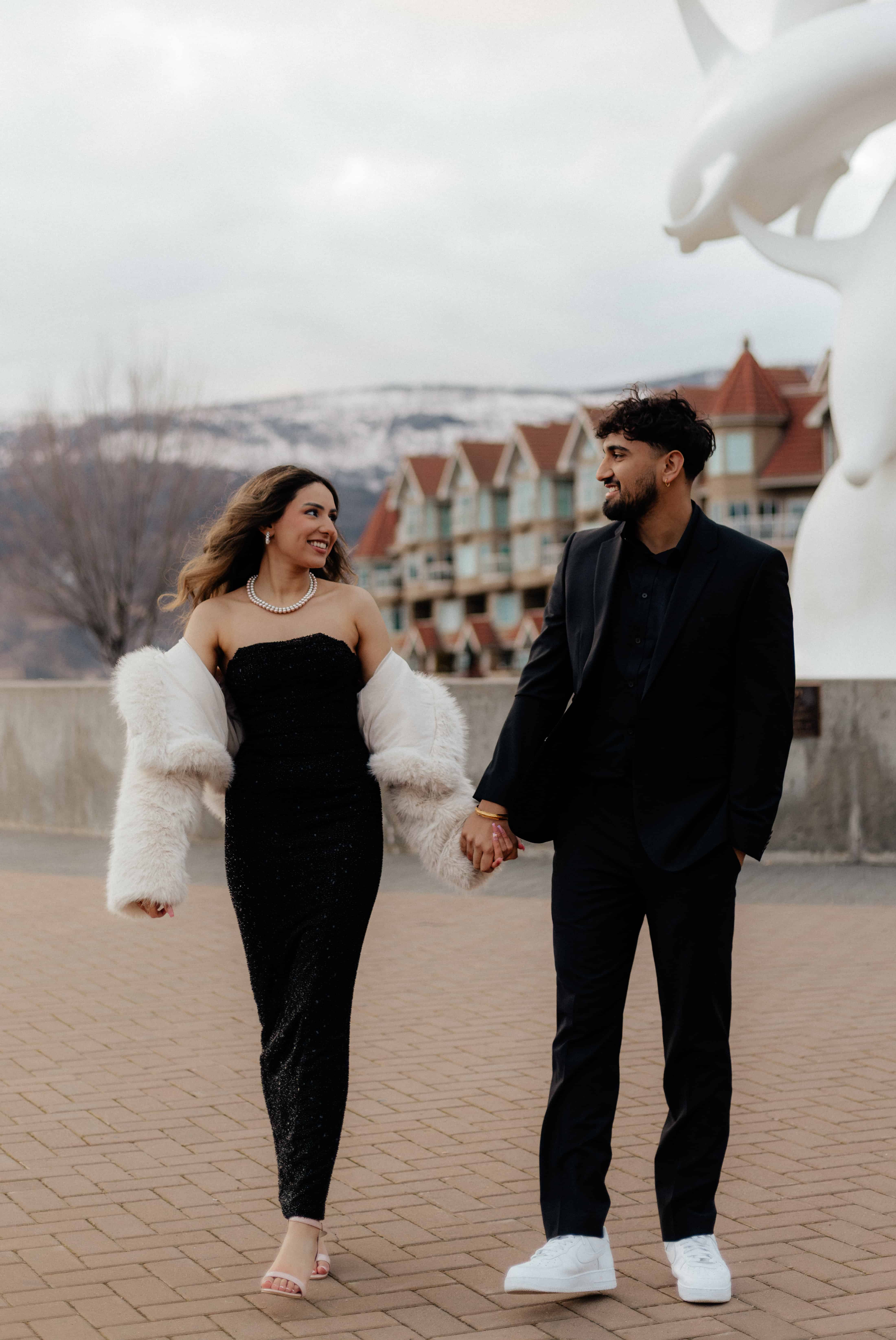 A couple walks hand-in-hand in downtown Kelowna in front of the Dolphins statue by Lake Okanagan