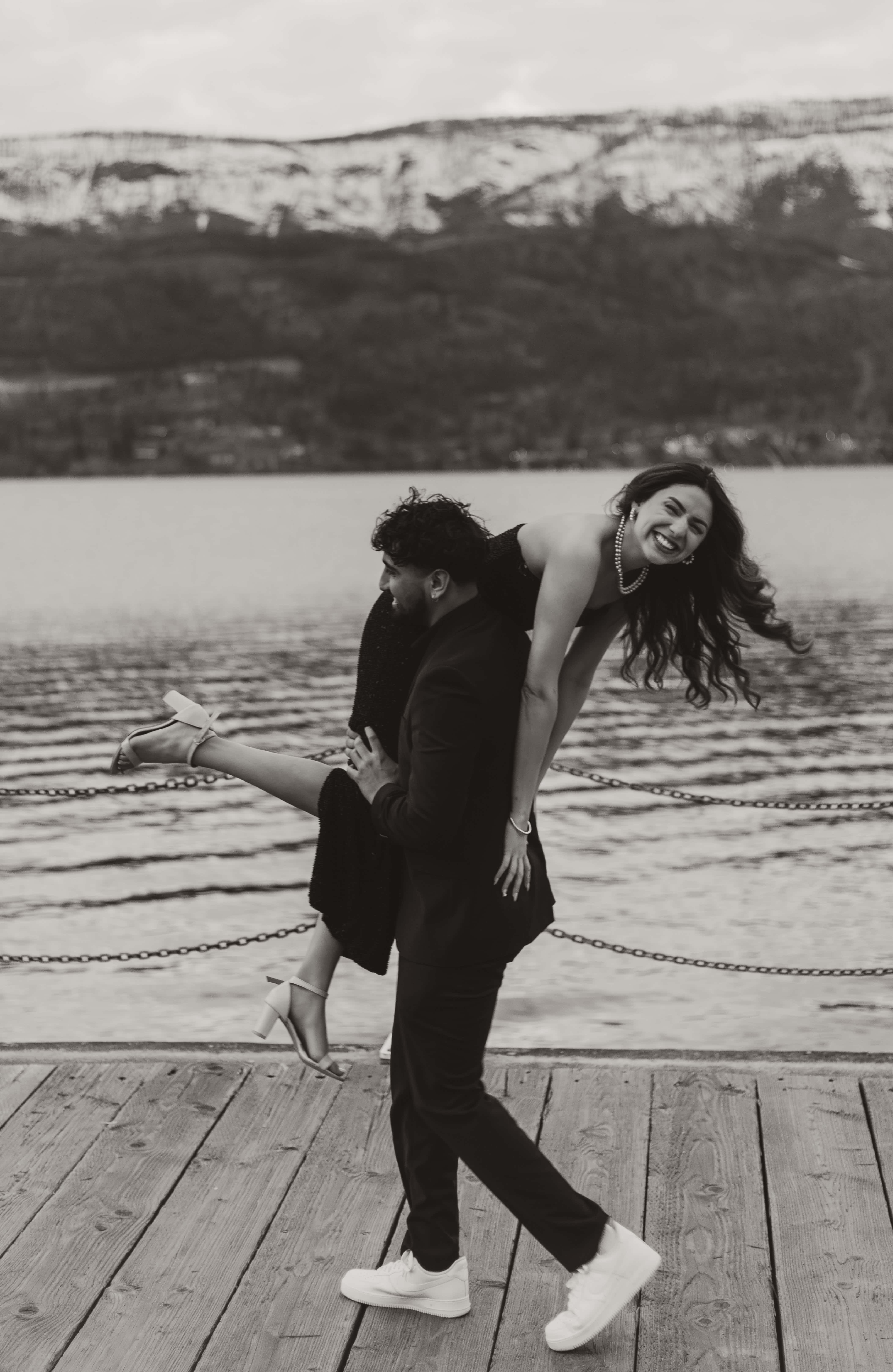 A man walks along the boardwalk of Lake Okanagan in Kelowna with his girlfriend over his shoulder as they laugh