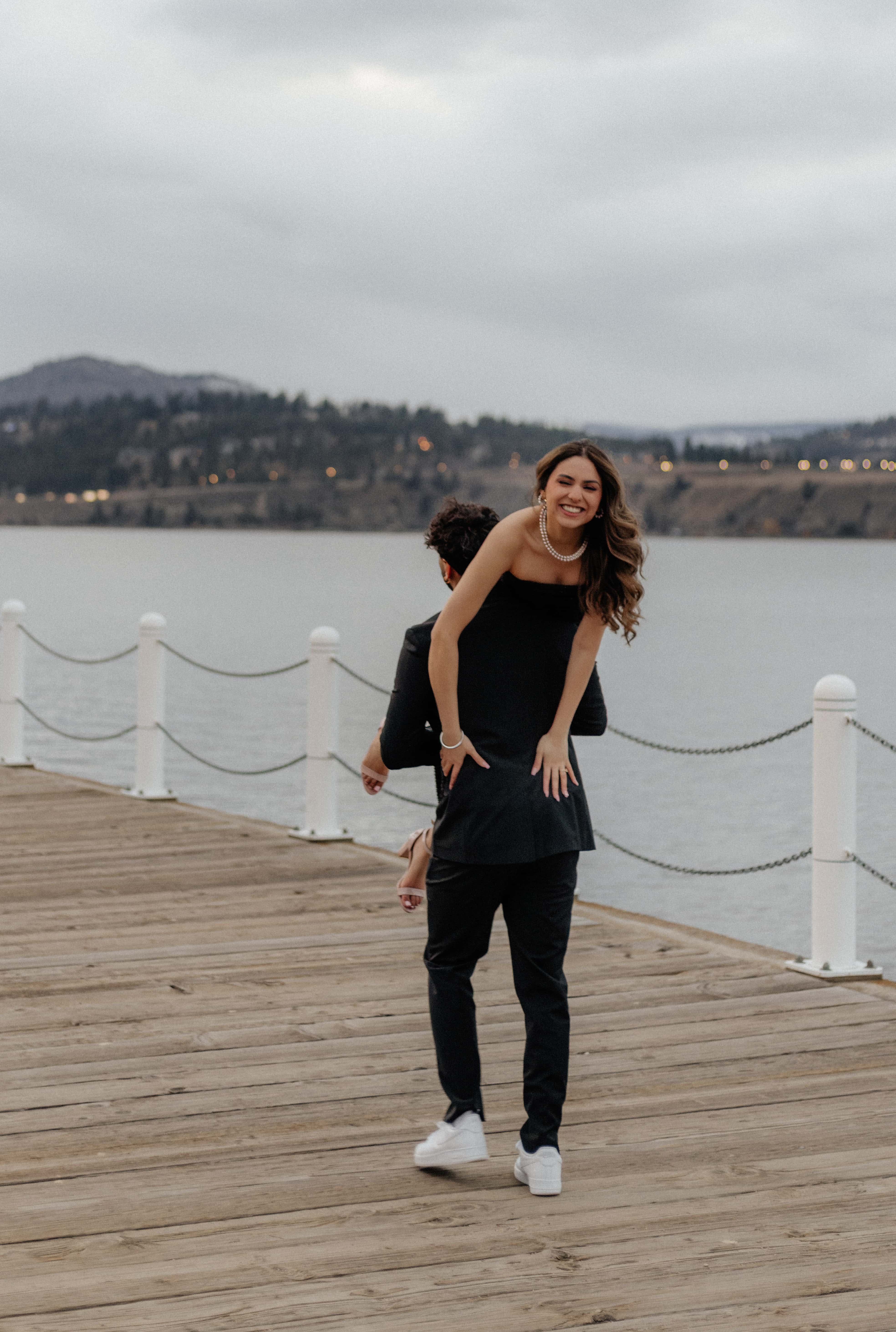 A man walks along the boardwalk of Lake Okanagan in Kelowna with his girlfriend over his shoulder as they laugh