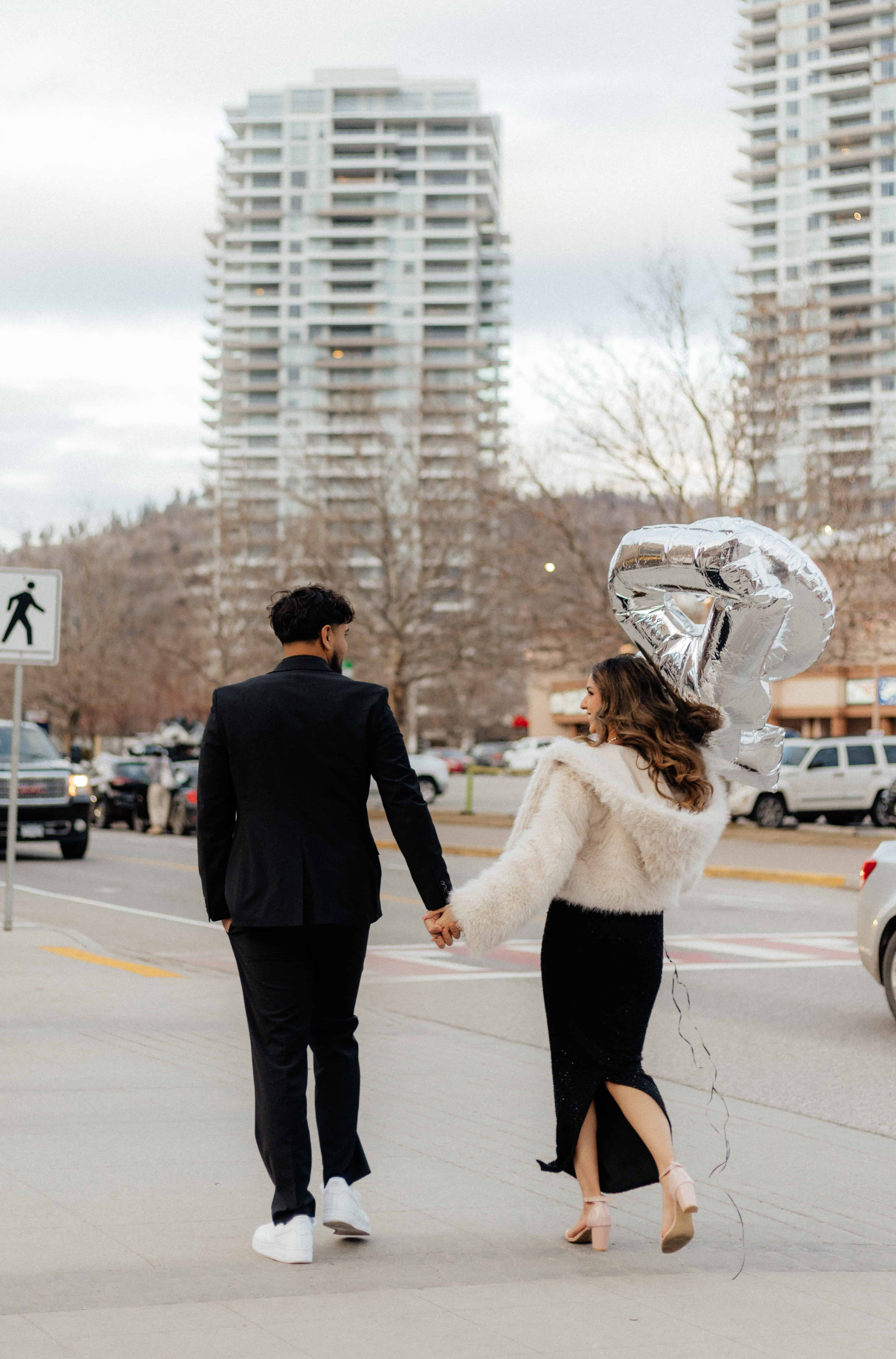 A couple walks hand in hand down the sidewalk during their downtown photoshoot in Kelowna, BC