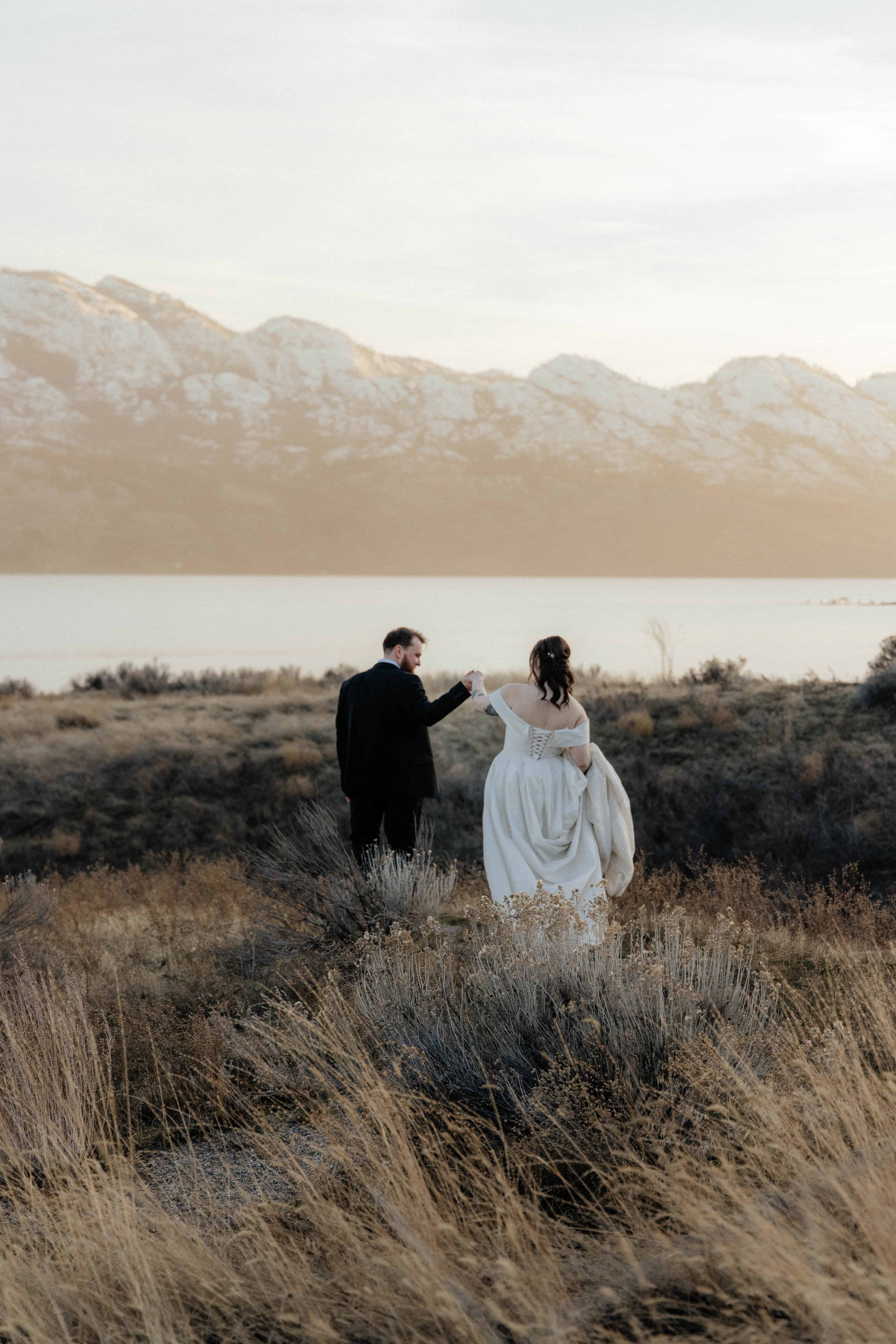 A groom guides his bride out to wander the fields of Sanctuary Gardens during their elopement at sunset, overlooking Lake Okanagan
