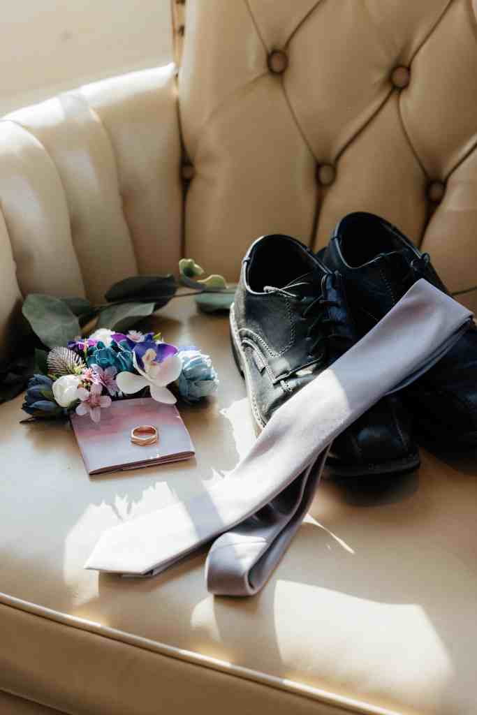 A detail shot of a groom's accessories including shoes, tie, boutonniere, and wedding ring