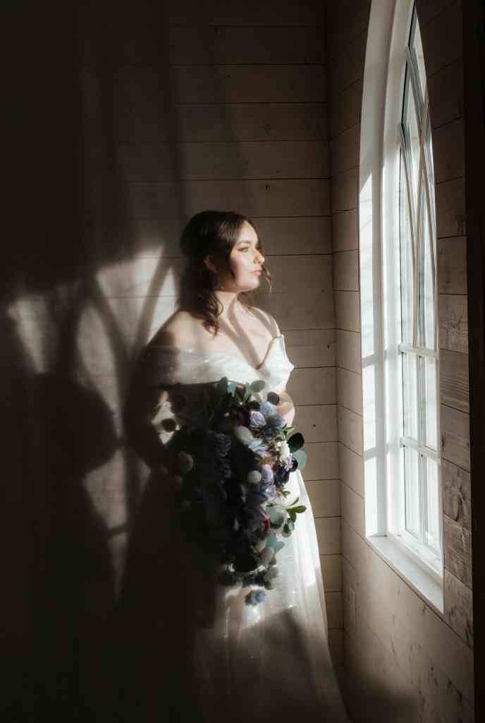 A beautiful, moody portrait of a bride in front of the light of an ornate window at Sanctuary Gardens, West Kelowna