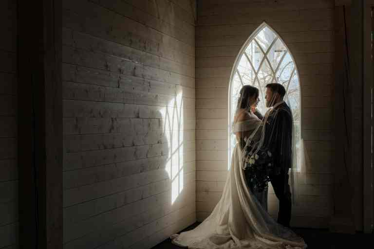 A gorgeous moody wedding portrait of a bride and groom basking in the light of an ornate window before eloping at Sanctuary Gardens, West Kelowna