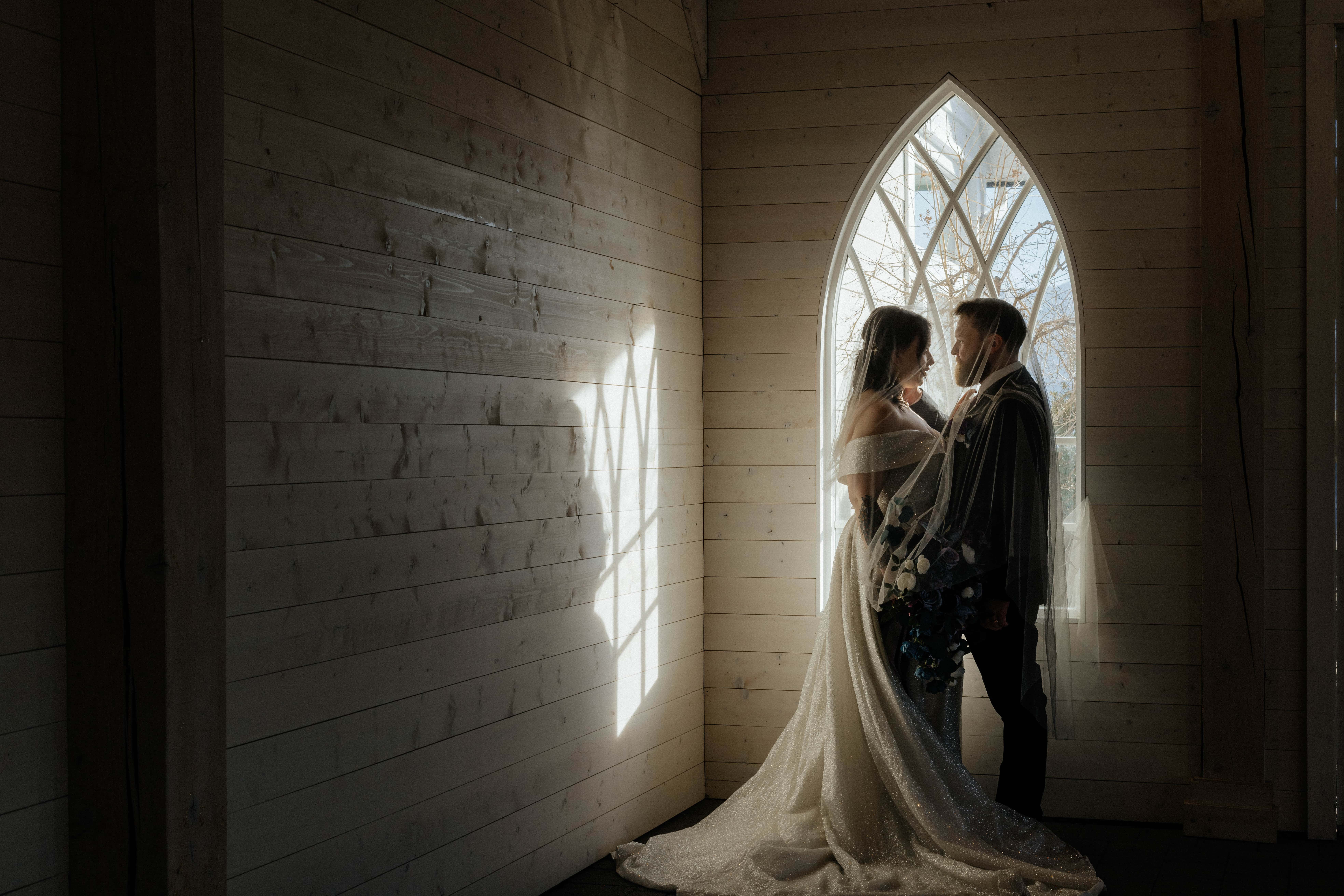 A gorgeous moody wedding portrait of a bride and groom basking in the light of an ornate window before eloping at Sanctuary Gardens, West Kelowna
