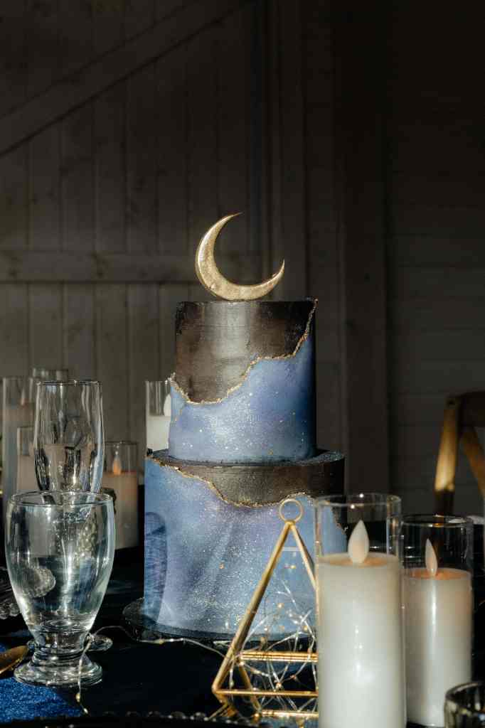A photo of a gorgeous celestial-themed wedding cake topped with a golden crescent moon for a wedding reception at Sanctuary Gardens, West Kelowna