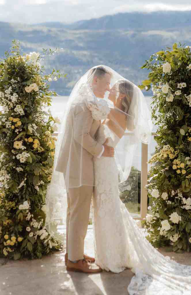 A newlywed bride and groom share a kiss under the bride's veil in the sunshine at their wedding in Lake Country, BC.