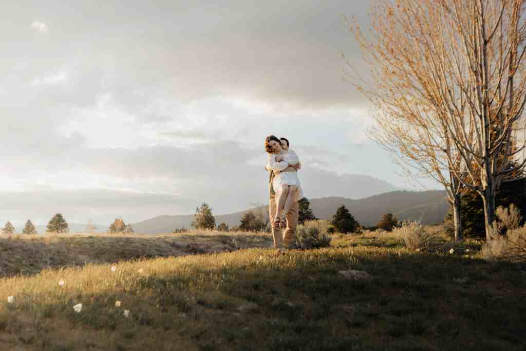 A couple plays around in an open field at golden hour during their engagement session at Sanctuary Gardens in West Kelowna BC