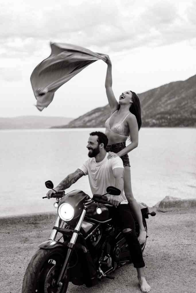A couple posing, laughing and having fun with their motorcycle in front of Lake Okanagan in Kelowna, BC