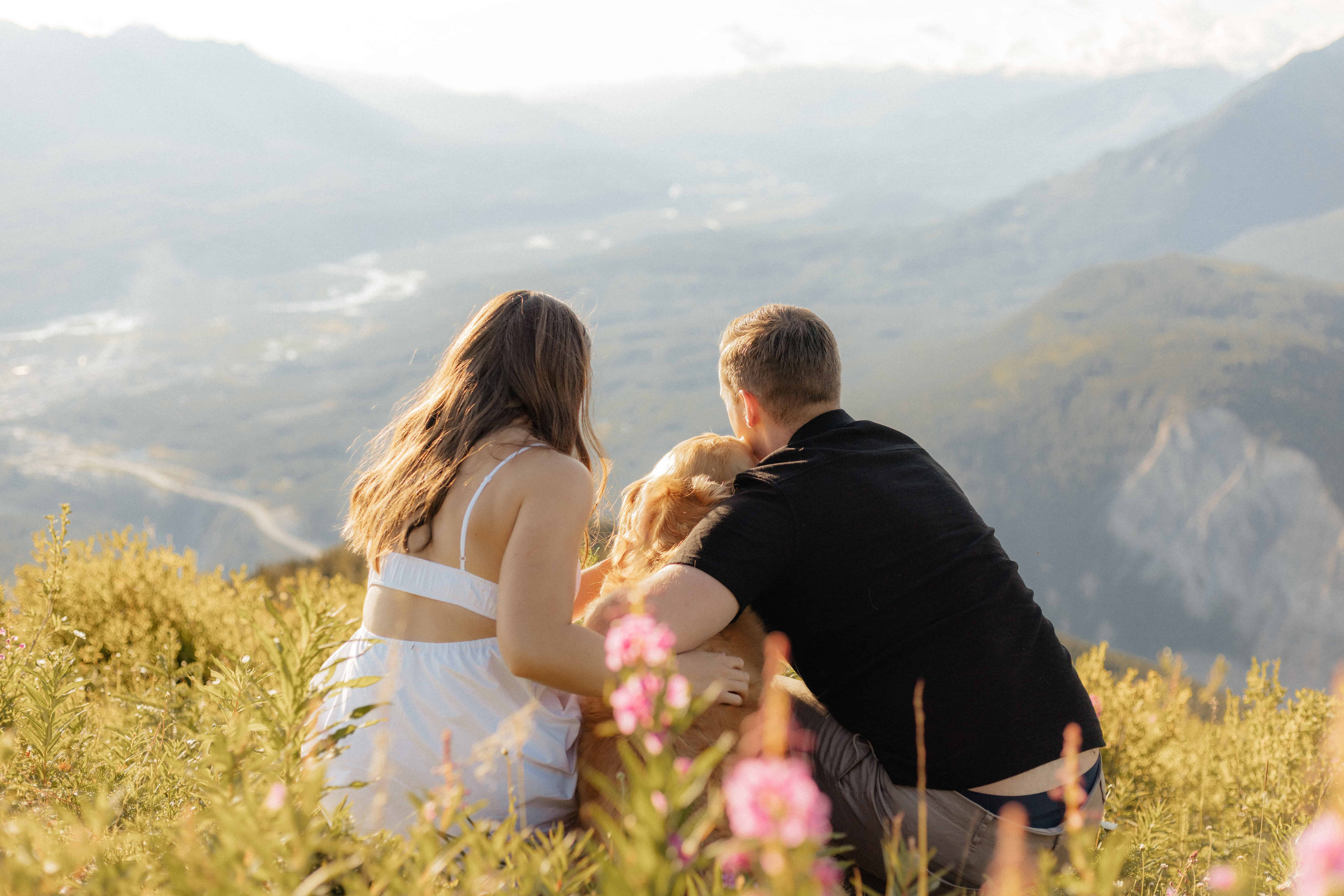 A couple enjoys a mountain top view with their dog during their engagement session on top of Mount 7 in Golden, BC